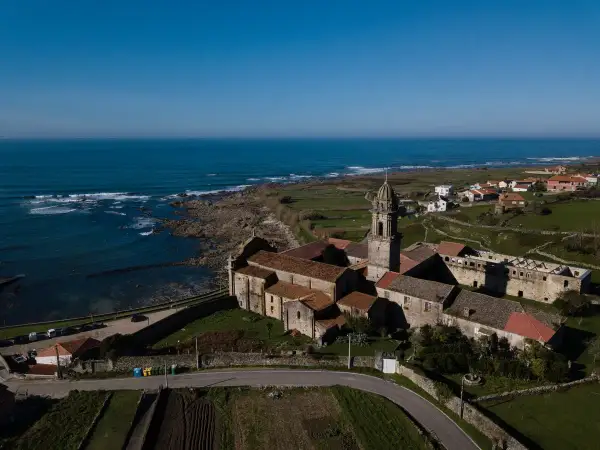 Monasterio de Santa María de Oia, con su torre campanario y tejados rojizos, se alza majestuoso junto al mar Cantábrico.