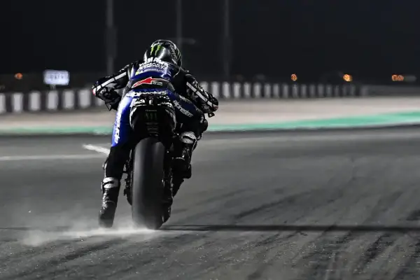 Piloto de MotoGP en plena acción, buscando el holeshot. La moto levanta polvo al acelerar en la noche.