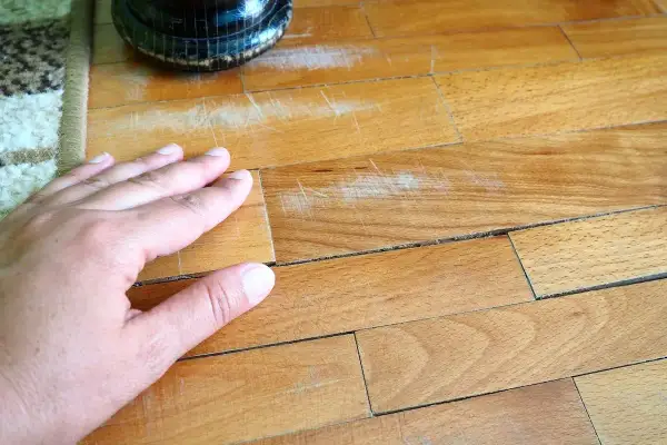 Mano sul parquet graffiato, un problema comune per chi vuole sapere come togliere strisciate scarpe dal parquet.