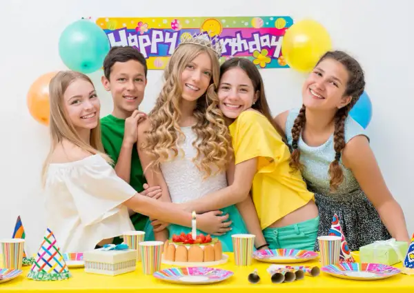 Uśmiechnięci nastolatkowie świętują urodziny przy stole pełnym balonów i tortu. W tle baner "Happy Birthday". Idealne konkursy zabawy na 50 urodziny!