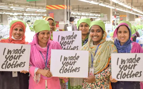 Frauen in einer Fabrik halten Schilder mit "I made your clothes". Dies unterstreicht die Bedeutung der Fair Wear Foundation für faire Arbeitsbedingungen.