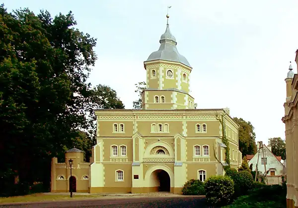Pałac w Golejewku, z charakterystyczną wieżą i bramą wjazdową, otoczony zielenią.