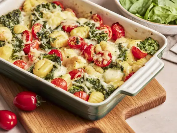 Gnocchi Spinat Auflauf mit Kirschtomaten und geschmolzenem Käse in einer grünen Auflaufform.