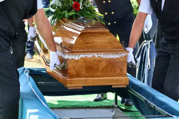 Tragarze w białych rękawiczkach niosą drewnianą trumnę. Nawet bez ubezpieczenia, zasiłek pogrzebowy na nieubezpieczonego członka rodziny jest możliwy.