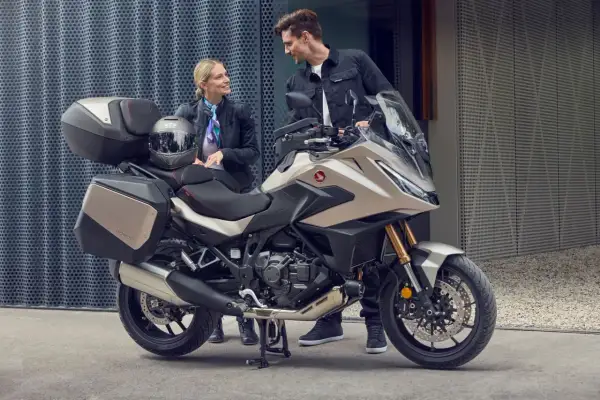 Pareja sonriente junto a una Honda NT 1100, lista para viajar. Opiniones positivas sobre su comodidad y diseño.