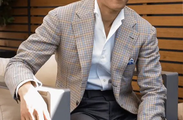 Uomo con giacca a quadri marrone, blu e arancione, camicia bianca e fazzoletto blu. Collezione drop 4.