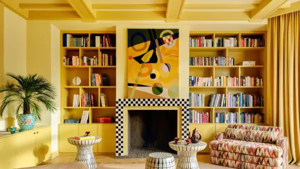 Ein Wohnzimmer in einem gelben Farbrausch, mit Bücherregalen, einem Kamin und einem bunten Sofa.