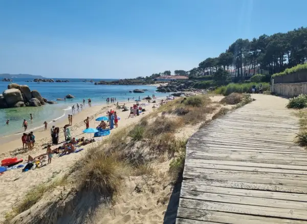 Gente disfrutando del sol y el mar en la playa Pedras Negras. Un camino de madera bordea la arena dorada y las dunas.