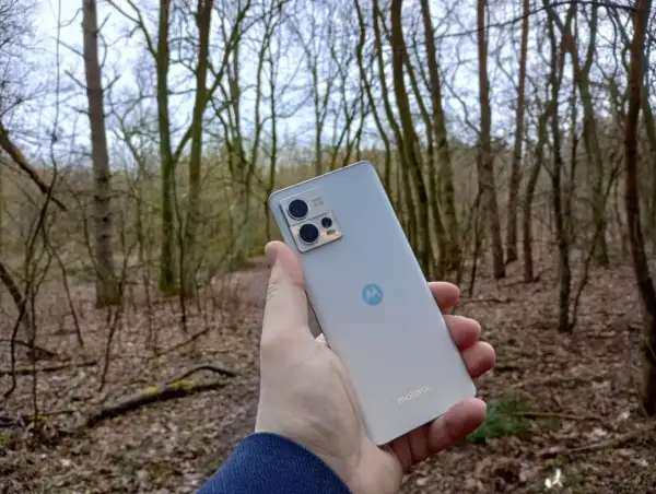 Dłoń trzyma srebrny smartfon Motorola G13 na tle lasu. Sprawdź motorola g13 dane techniczne, by poznać jego możliwości.