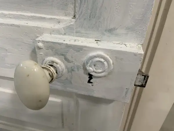 Poignée de porte ancienne recouverte de peinture blanche écaillée. Le mécanisme de serrure est visible, prêt à enlever peinture sur poignée de porte.