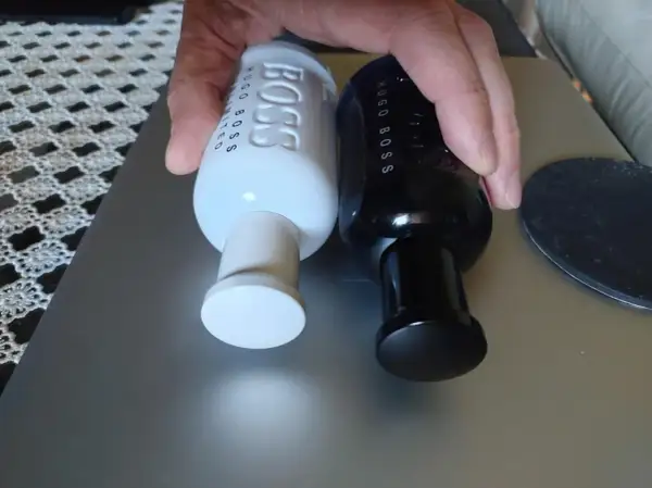 Dwie butelki perfum Hugo Boss, jedna biała męska, druga czarna, leżą obok siebie.
