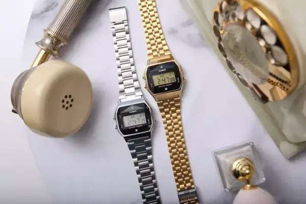 Dwa zegarki Casio, srebrny i złoty, obok retro telefonu. Idealne dla kobiet ceniących styl, często pojawiają się w rankingach luksusowe zegarki damskie ranking.