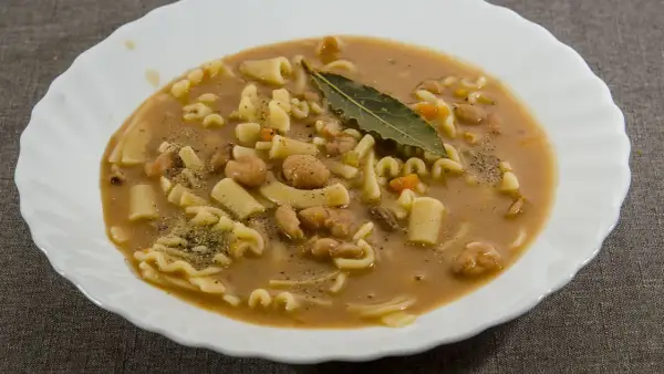 Un piatto fumante di pasta e fagioli, con pasta corta, fagioli borlotti, carote e una foglia di alloro.