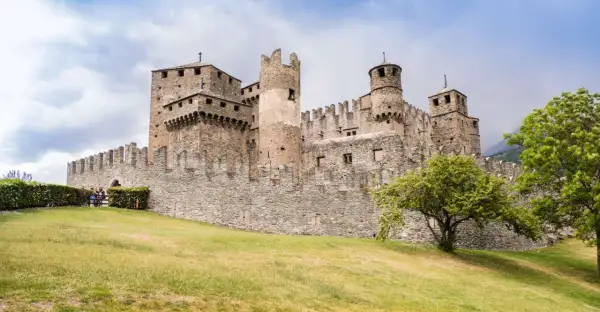 Imponente castello medievale, uno dei borghi Valle d'Aosta più suggestivi, con torri merlate e mura in pietra su un prato verde.