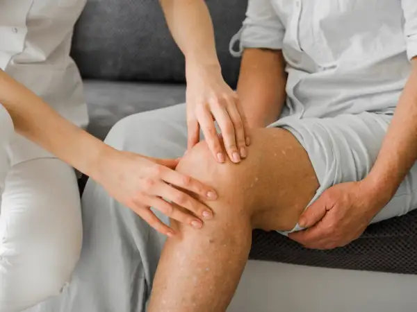 Lekarz bada nogę pacjenta z widocznymi żylakami. Czy skleroterapia jest bezpieczna? To pytanie nurtuje wiele osób.