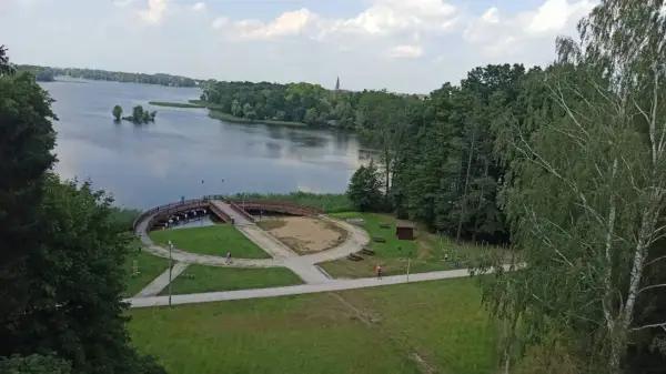 Malowniczy widok na jezioro i promenadę w Szczecinku. Widać ścieżki idealne na rowerowy spacer, mostek i zieleń.