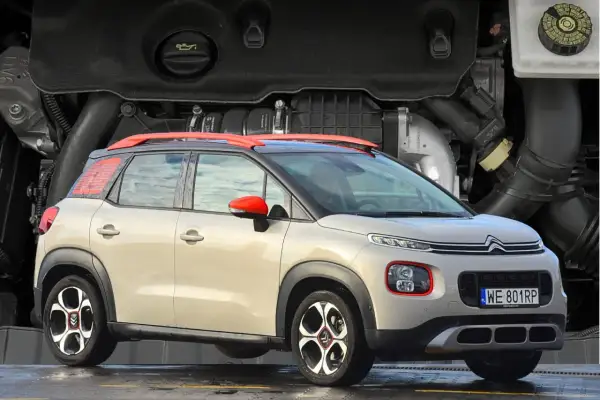 Nowy Citroen C3 2025 w beżowym kolorze z czerwonymi akcentami, prezentowany na tle silnika.