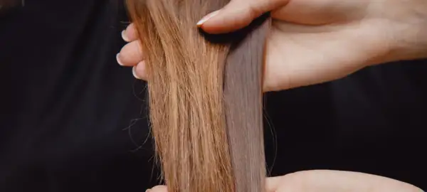 Hände halten zwei Strähnen Haar, eine glänzend, die andere matt und glanzlos.