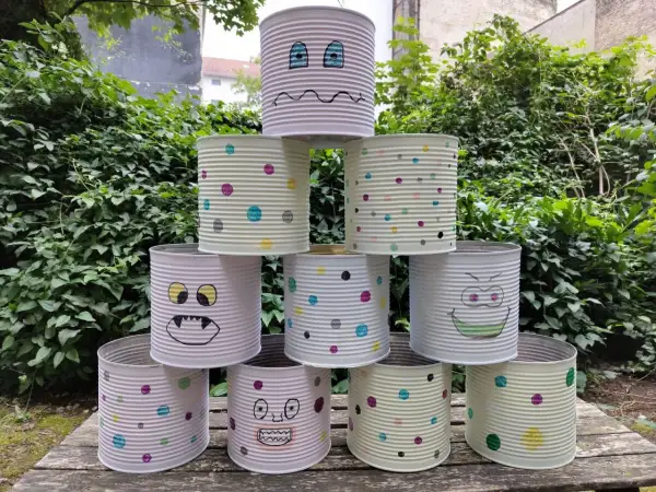Kreatives Recycling mit Kindern: Dosen-Monster-Turm im Garten. Bunte Punkte und lustige Gesichter machen aus alten Konserven ein Spiel.
