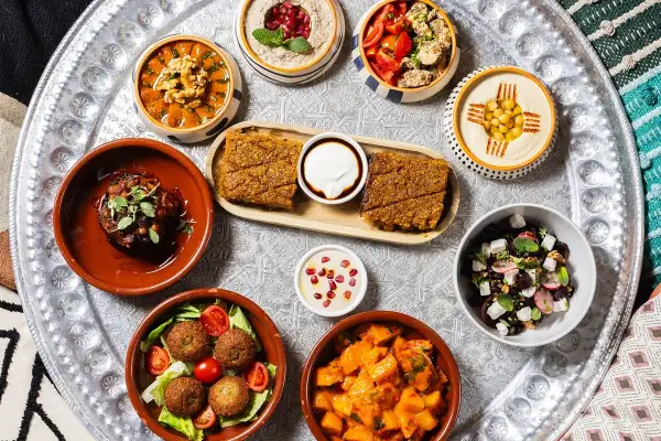 Un vassoio con diverse pietanze mediorientali, perfetto per scoprire dove mangiare a Milano. Hummus, falafel, insalate e spezzatini invitano a un viaggio di sapori.