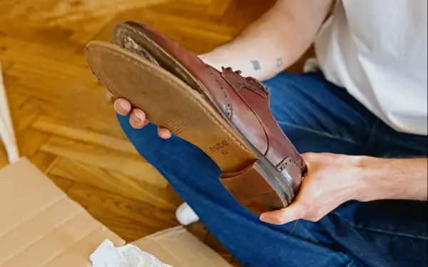 Une personne examine une chaussure en cuir marron, montrant l'usure de la semelle.