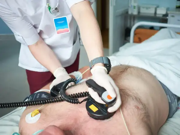 Ratownik medyczny wykonuje kardiowersję pacjentowi leżącemu w łóżku szpitalnym.