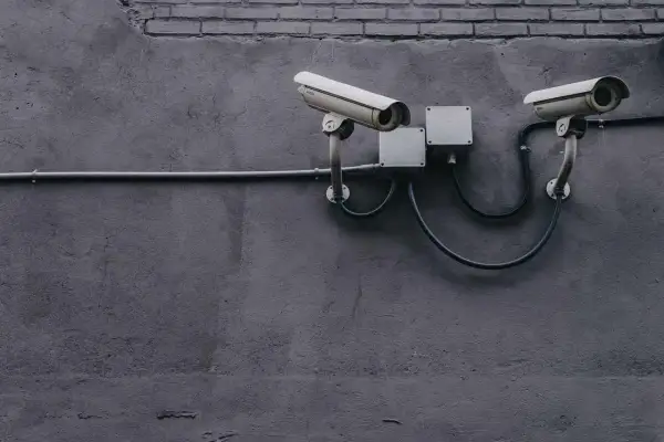 Dwie kamery monitoringu na szarej ścianie, podłączone do puszek elektrycznych. Zapewniają bezpieczeństwo i monitoring w domu.