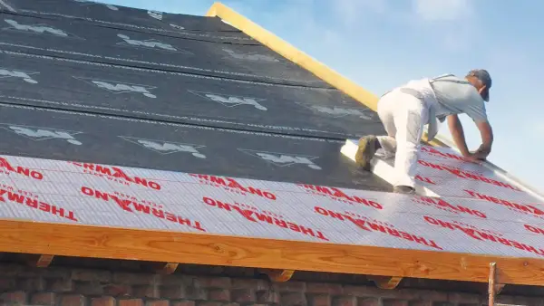 Pracownik montuje izolację nakrokwiową na dachu, układając warstwy materiału termoizolacyjnego.