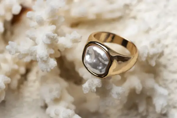 Anillo de oro amarillo con perla irregular sobre coral blanco. La diferencia entre oro blanco y oro amarillo es evidente en su brillo.
