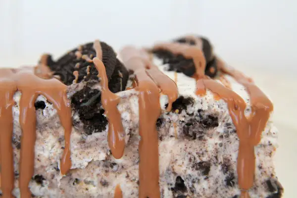 En bit krämig oreo cheesecake med chokladsås som rinner ner.