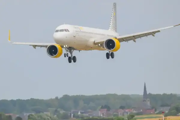 Samolot hiszpańskich linii lotniczych Vueling z żółtymi gondolami silników zbliża się do lądowania nad malowniczą miejscowością.