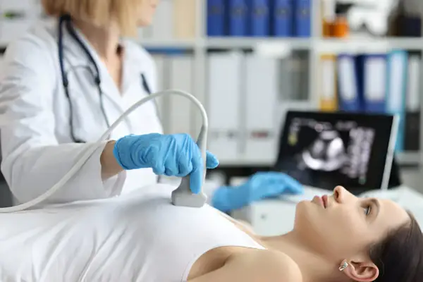 Lekarka wykonuje badanie USG piersi, by wyjaśnić wątpliwości po mammografii. Obraz z monitora pokazuje szczegóły.