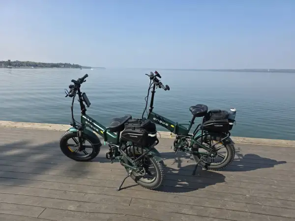 Dwa zielone rowery elektryczne z sakwami, gotowe na wyprawę z zasięgiem 200 km nad spokojną wodą.