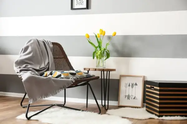 Un angolo accogliente con sedia, cuscino decorativo e tulipani gialli. Ispirazione per come dipingere le pareti di casa con strisce grigie e bianche.