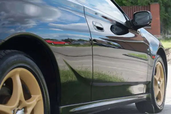 Błyszczące czarne uni auto z złotymi felgami odbija niebo i otoczenie.