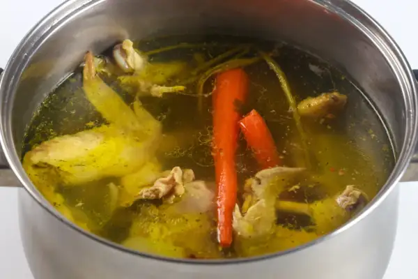 Gotowanie rosołu pod przykryciem to sekret głębokiego smaku. Widać kawałki kurczaka, marchewkę i przyprawy w bulionie.
