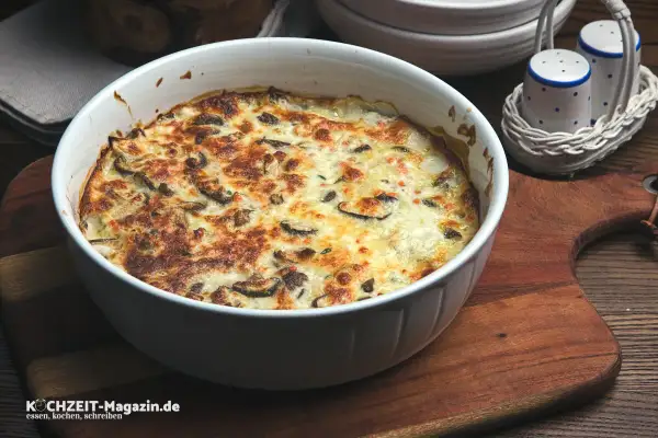 Herzhafter Kohlrabi-Auflauf mit Pilzen und Käse überbacken, serviert in einer weißen Auflaufform auf einem Holzbrett.