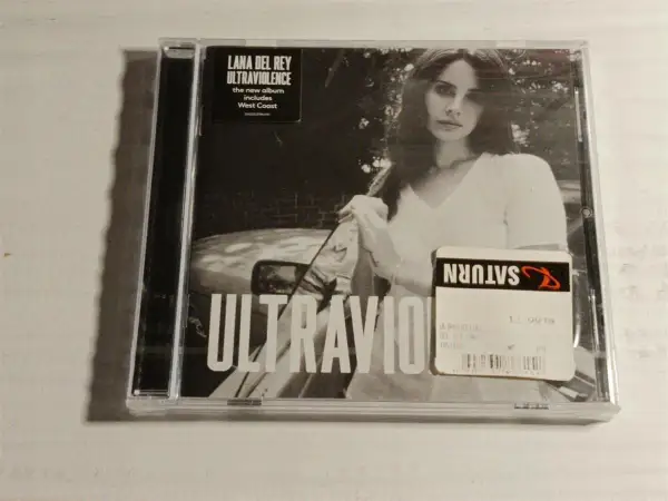 Okładka płyty Lana Del Rey Ultraviolence. Na czarno-białym zdjęciu artystka w białej koszulce, obok naklejka Saturn z ceną.