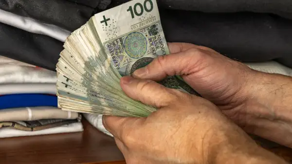 Dłonie trzymające plik banknotów 100 zł. To jeden z elementów, który wpływa na narzędzia polityki pieniężnej.