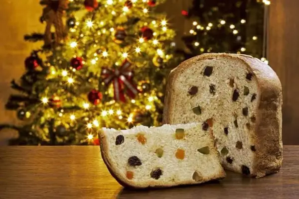 Un panettone, symbole de Noël, avec sa tranche coupée révélant fruits confits et raisins secs. Son origine italienne se célèbre devant un sapin illuminé.