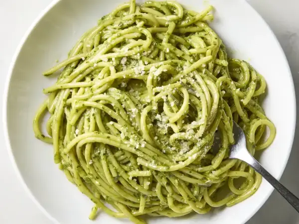 Pyszny makaron z pesto, posypany parmezanem, czeka na widelcu. Idealny na szybki obiad.
