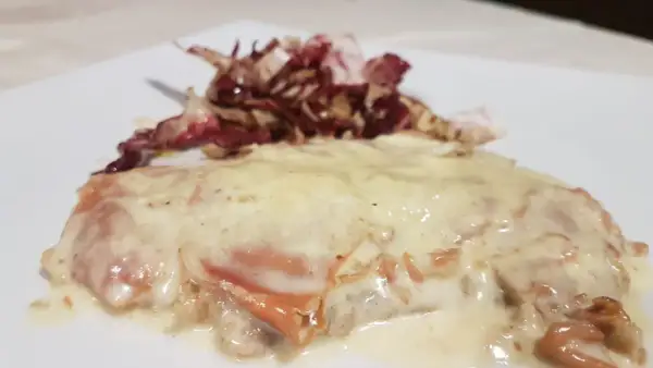 Deliziosa cotoletta alla bolognese, dorata e ricoperta da una cremosa salsa, accompagnata da radicchio croccante.