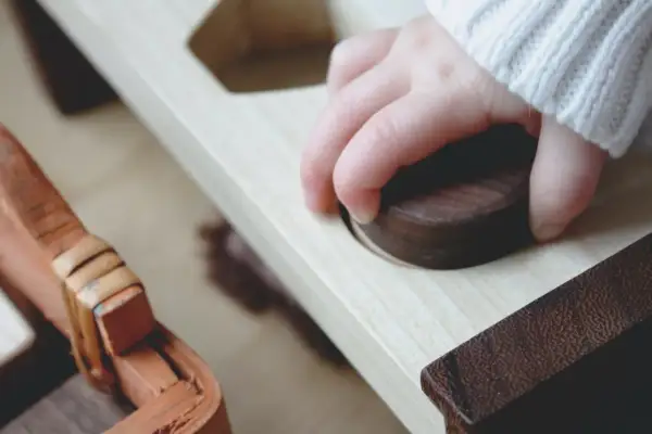 Mano de niño explorando un juguete de madera, un ejemplo del método Montessori para el desarrollo sensorial.