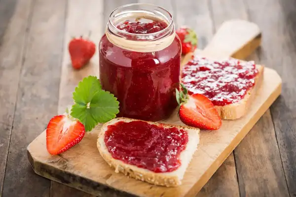 Marmellata di fragole fatta in casa con il Bimby, spalmata su fette di pane fresco, con fragole intere e a metà.