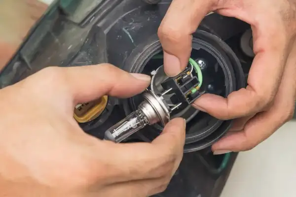 Wymiana żarówki przód Opel Corsa C. Dłonie montują nową żarówkę w reflektorze.