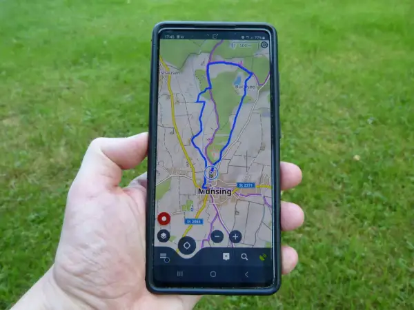 Hand hält Smartphone mit einer Wanderwege App, die eine Route bei Munsing anzeigt. Perfekt für die nächste Tour!