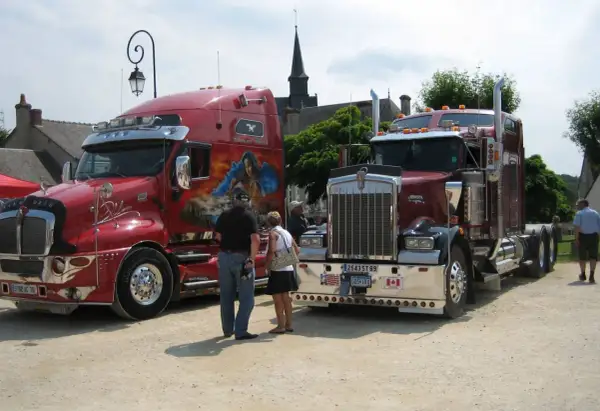 Deux camions américains tuning, l'un rouge vif avec une peinture personnalisée, l'autre bordeaux, se dressent fièrement.