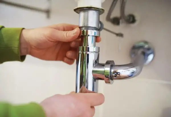 Mains pour démonter un siphon de lavabo, une étape clé pour savoir comment déboucher.