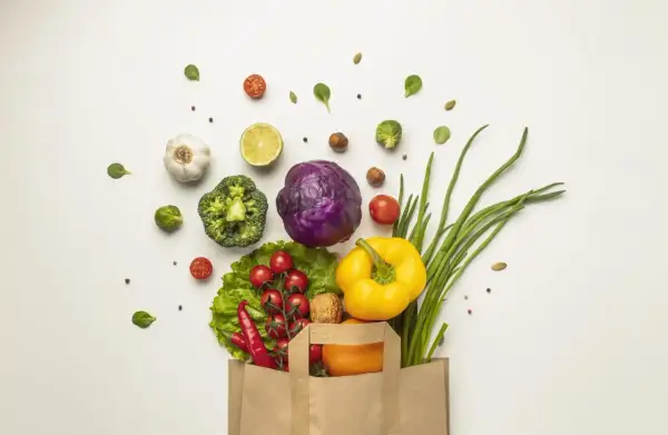 Bolsa de papel llena de verduras frescas: brócoli, col morada, pimientos, cebolletas, tomates, chiles, ajo, limón y una naranja. ¡Perfecto para 100 comidas!
