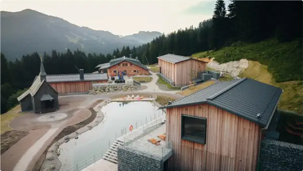 Idyllische hotels auf dem berg mit kleinem See und Kapelle, umgeben von Wald und Bergen.
